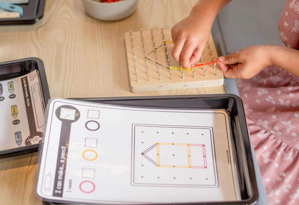 A preschooler stretching rubber bands across a wooden geoboard during a math and STEM activity at Hope Kids Preschool