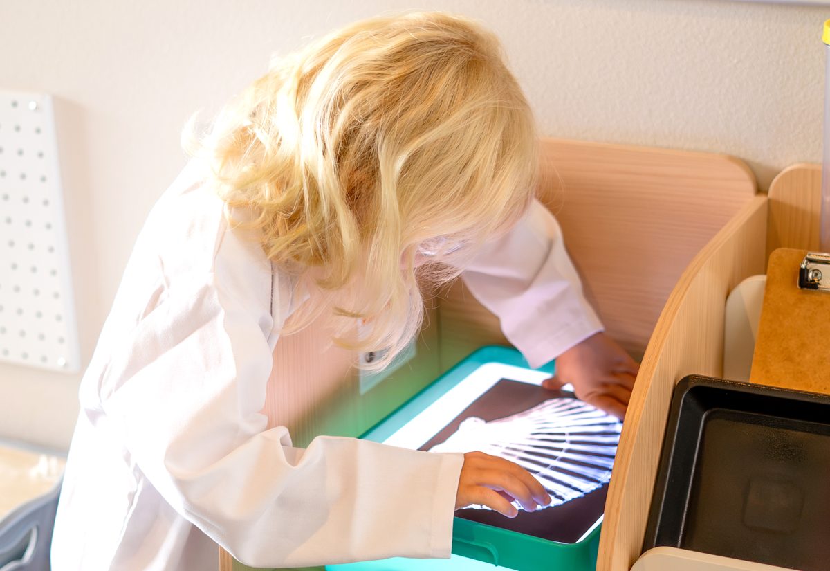 A preschooler in a lab coat examining x-ray images on a light table during a science activity at Hope Kids Preschool
